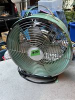 Front and slight side view of the retro style table fan showing its metal blades, protective grille, green metal casing and carrying handle on top