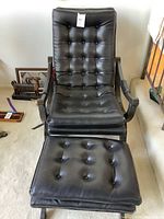 Front view of black naugahyde chair and ottoman showing tufted button upholstery and wood frame