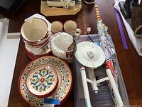 Bobby Flay ceramic dish set including bowls, plates, 2 mugs, and a large umbrella and other miscellaneous items on a table.