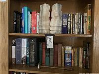 Two shelves displaying assorted books and two carved stone bust-shaped bookends with a metal candle snuffer placed on the bottom shelf.