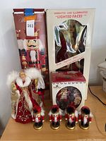 Lot including boxed animated Christmas lighted face doll, five nutcracker figurines, and a Christmas decorative doll with red and gold gown and feathered wings.
