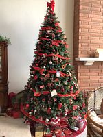 Full view of 10 foot decorated artificial Christmas tree with red ribbons, bows, ornaments, skirts at base and several gift bags and boxes beneath