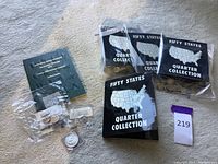 Top-down photo showing multiple Fifty States Quarter Collection folders and a green coin folder with mixed loose coins in plastic bags.