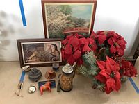 Photo showing framed prints, assorted decor, stein, horse figurine, stone sculpture, candles, and artificial poinsettias arranged on floor.