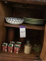 Shelf with green floral plates stacked and Delft hand painted bowl with blue floral pattern on top. Below shelf are red house Christmas ornaments, a clear jar, and beaded napkin holders.