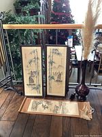 Photo of two framed bamboo and boat pictures, scroll picture on floor, tall purple glass vase with pampas plumes near furniture and Christmas tree.
