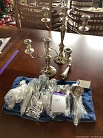 Photo showing two silver-plated candelabra and multiple pieces of flatware in plastic wrap on a blue cloth bag on a wooden table.