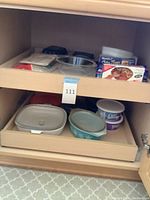 Cabinet shelf with various Pyrex and plastic food storage containers and boxes of plastic bags
