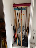 Photo showing multiple garden tools including brooms, rakes, shovels, and cutters stored in a white cabinet or closet.