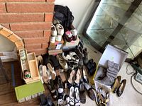 Wide shot of multiple pairs of men's and women's shoes arranged on floor next to fireplace and glass cabinet with sewing items in wooden box on left.