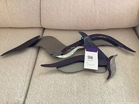 Two metal bird wall art pieces arranged on a couch showing their shape and size.