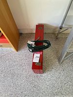 Red metal carrying case with white Milwaukee Heavy-Duty Sawzall branding and a green extension cord coiled on top.