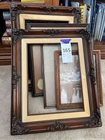 Four decorative frames arranged on floor, showing two large ornate carved wood frames with cream borders and two smaller plain wood frames.