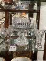 Photo of crystal cake stand with pedestal, crystal vase, and four wine glasses on glass shelf