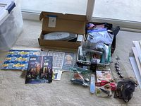 Overview of lot on beige carpet showing stamps, jewelry, ThermaPulse device box, and various miscellaneous items spread out