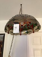 Side view of the hanging light fixture showing detailed dragonfly stained glass motif and metal chain suspension.