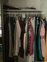 Photo of women's clothing on hangers showing jackets, skirts, dresses, blouses, pants in various colors and fabrics on hangers in a closet.