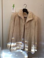 Front view of cream mink fur coat hanging on black hanger against white wall