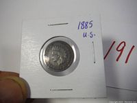 Front (obverse) side of the 1885 US Indian Head penny coin showing Lady Liberty profile wearing an Indian feather headdress held in a white cardboard display holder.