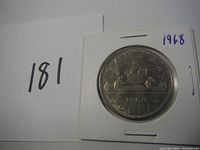 Front side of the 1968 Canadian silver dollar coin showing the sailing ship and the year '1968' handwritten on the holder.