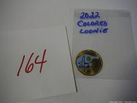 Photo of the 2022 colored loonie coin in protective packaging labeled '2022 Colored Loonie' with lot number 164 on white paper.