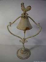 Front view of the cast iron bell with rooster figure and base, showing the overall design and some visible rust spots.