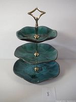 Full view of the 3-tier ceramic pottery tray with green-blue glaze and brass handle standing on white surface with a small number 8 card.