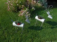 Two metal reindeer garden ornaments placed on grass with curly metal antlers and open cylindrical bodies holding faux greenery and red berries.