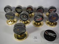 Photo showing 10 NHL hockey pucks each encased in a clear plastic capsule mounted on gold stands, with team logos visible.