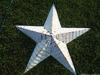 Large tin star painted white with visible rust and patina, shown lying on grass
