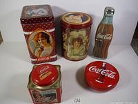 Five vintage Coca-Cola collectible tins arranged on a white surface, showing their front artwork and shapes.
