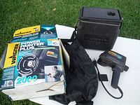 Complete view of Wagner Power Painter Plus 2000 paint sprayer with box, black carrying case, black protective cover, and various accessories including paint hose and user guide on grass.