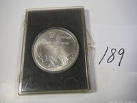 Photo of the front of the 1976 Montreal Olympics $10 hockey silver coin in protective case showing hockey players, Olympic rings, and inscriptions.