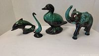 Four Blue Mountain style animal figurines set against white background: an elephant, swan, duck, and dolphin with green and black glaze