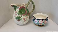 Set showing both Fitz and Floyd floral bowl and grape pitcher side by side.