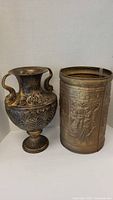 Both urns side by side showing design and size comparison, brass urn with handles and metal urn with embossed scenes