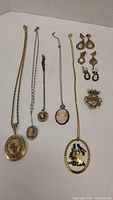 Photo showing multiple necklaces with cameo and porcelain pendants and several pairs of earrings.