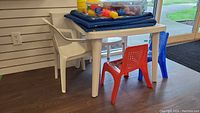 White plastic play table with four plastic chairs (white armchair, solid white chair, red and blue perforated back with character seat designs)