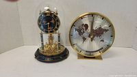 Both clocks together on a white background showing full items including the glass dome of the Kundo clock and the brass finish on the Birks clock