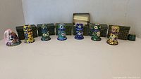 Six cloisonné toothpick holders arranged in a line with their boxes behind them and one cloisonné bell on the left side.