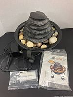 Front view of the Envirascape illuminated tabletop water fountain with power adapter, spare bulb packet, and instruction manual