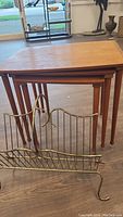 Three teak nesting tables nested together with brass magazine rack in front