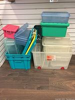 Full view of stacked plastic containers including large translucent containers with wheels, blue and green containers with lids, and red container with latch.
