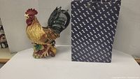 Front and side view of the colorful ceramic rooster pitcher with original branded Fitz and Floyd box beside it.