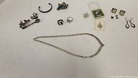 Overview of all silver jewelry items including necklace, multiple earrings, rings, and pins displayed on flat surface