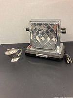 Front angled view of reproduction electric toaster with chrome diamond pattern and vintage silver lighter shaped like oil lamp