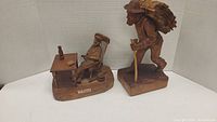 Two wood carvings: man sleeping in rocking chair beside a table and man walking carrying bundle of wood on back