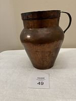 Front and side view of antique copper pitcher showing bulbous body and riveted handle