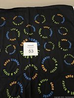 Black cotton scarf with colorful circular text patterns repeating 'Greg Curnoe' and 'Life & Stuff'