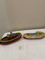 Full side view of two wooden folk art boats on white towel, tugboat on the left and towed smaller boat on the right